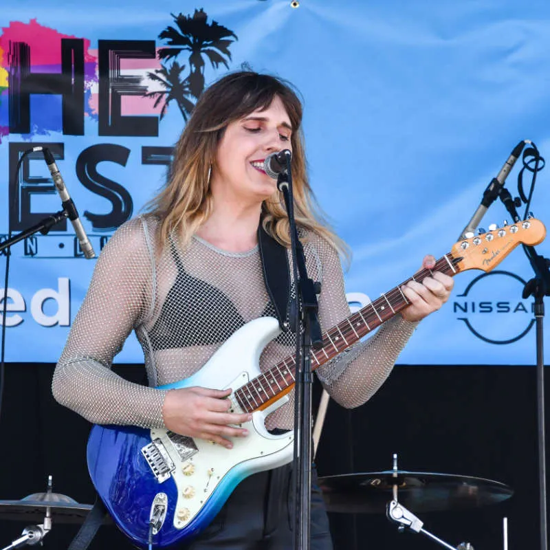 Mariela standing on a stage singing and playing her guitar.